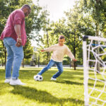 Pai e filho jogando futebol no gramado com tipos de grama resistentes ao tráfego de pessoas.